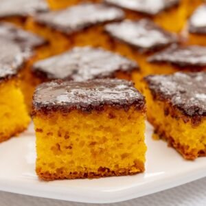 Close-up of moist carrot cake squares with chocolate glaze on a white plate.