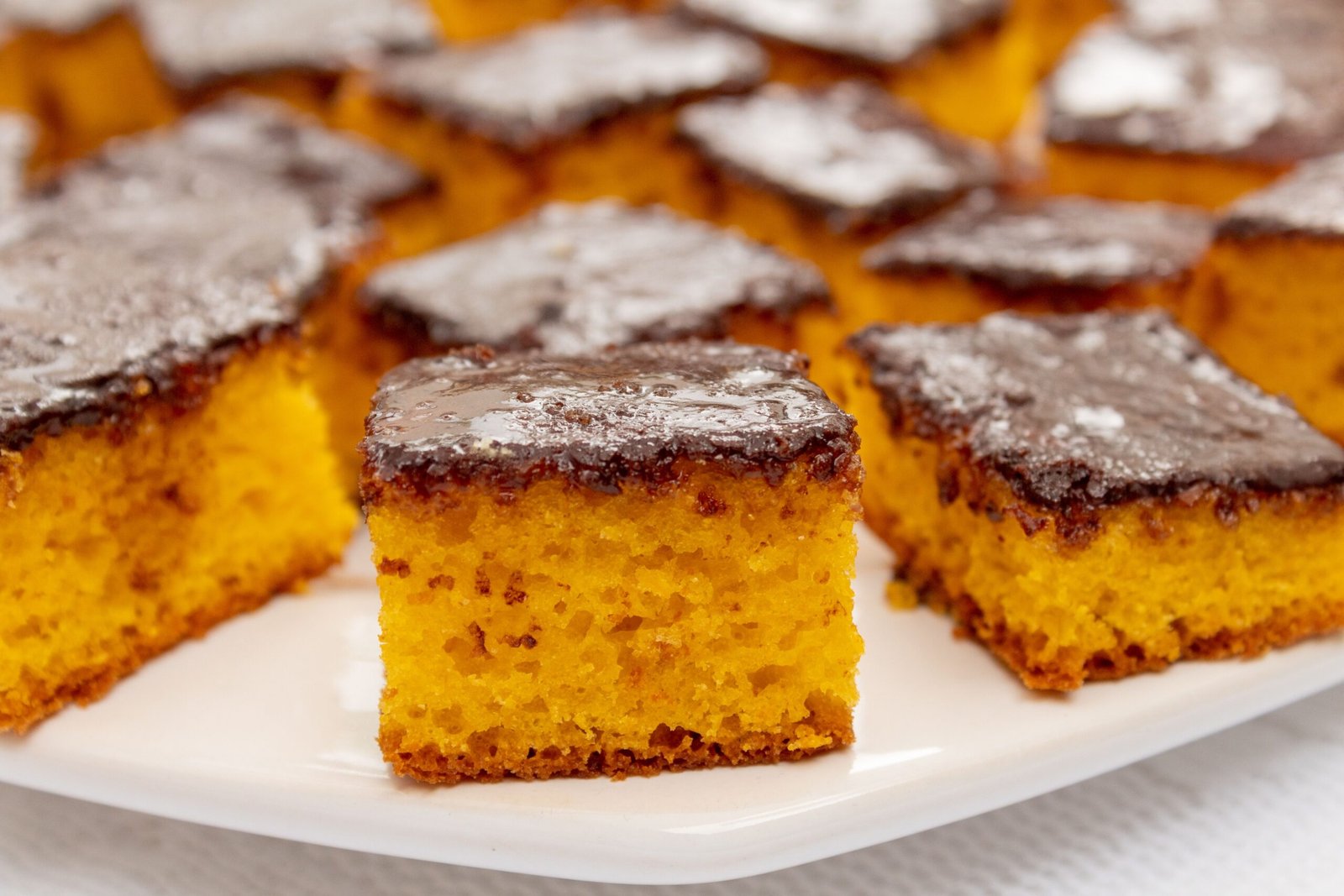 Close-up of moist carrot cake squares with chocolate glaze on a white plate.