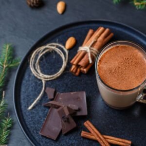 A warm glass of cocoa surrounded by cinnamon sticks, chocolate, and festive cookies.