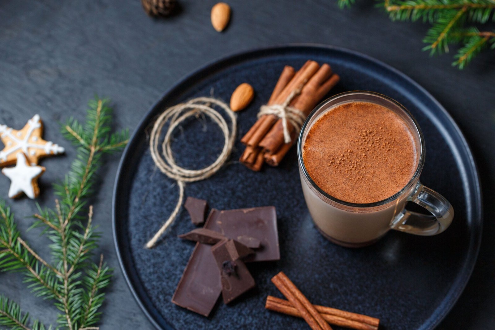 A warm glass of cocoa surrounded by cinnamon sticks, chocolate, and festive cookies.